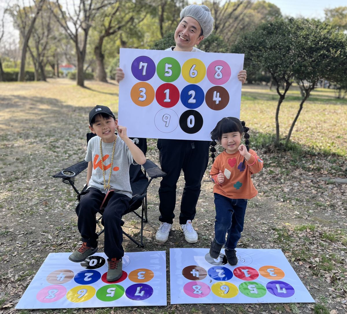 Brain Step のシートの図を掲げる開発者と、並べた2枚のシートの上に立つ女の子・いすに座って足をのせる男の子