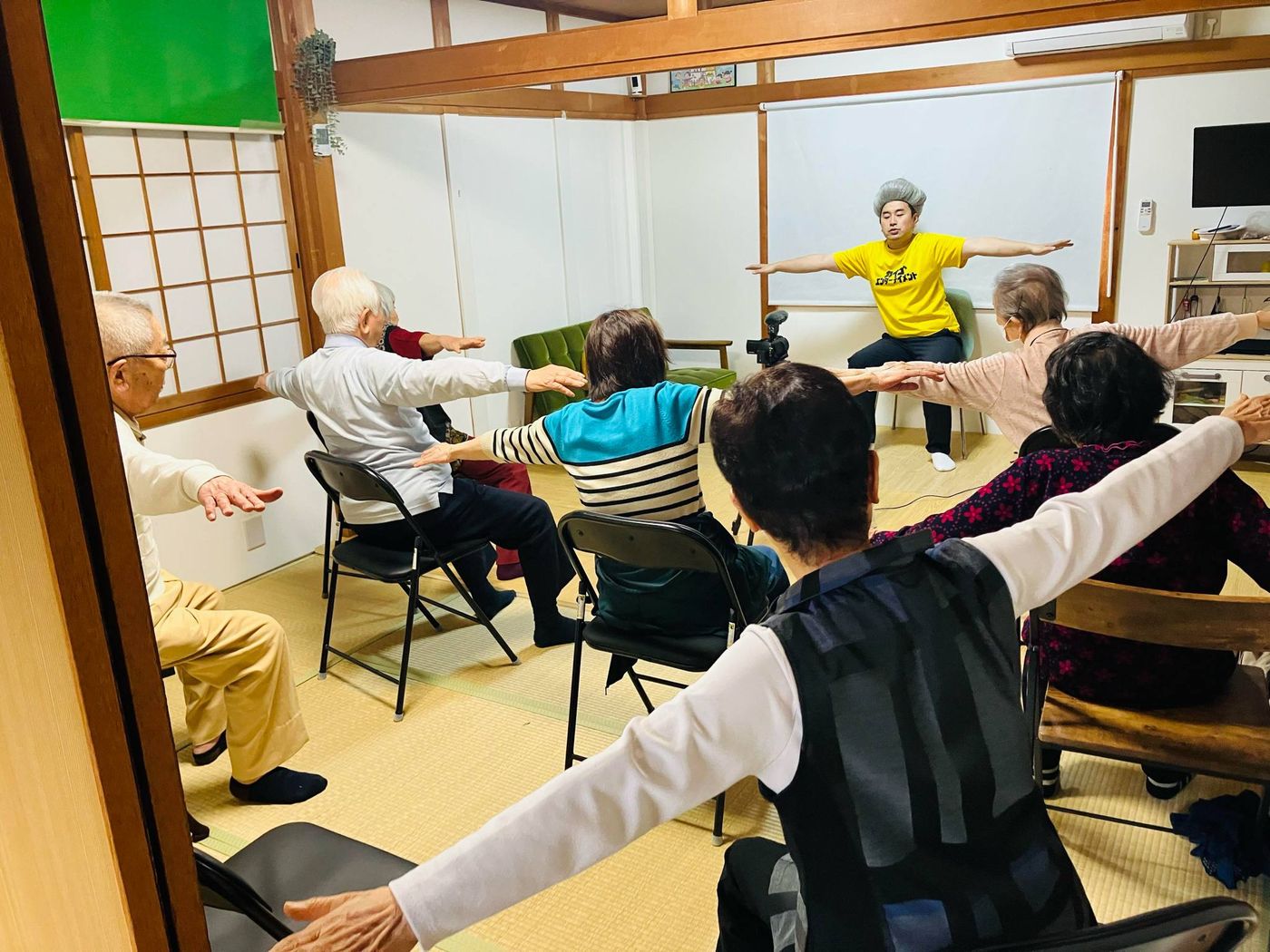 和室に椅子を並べ、参加者が両手を横に広げている様子