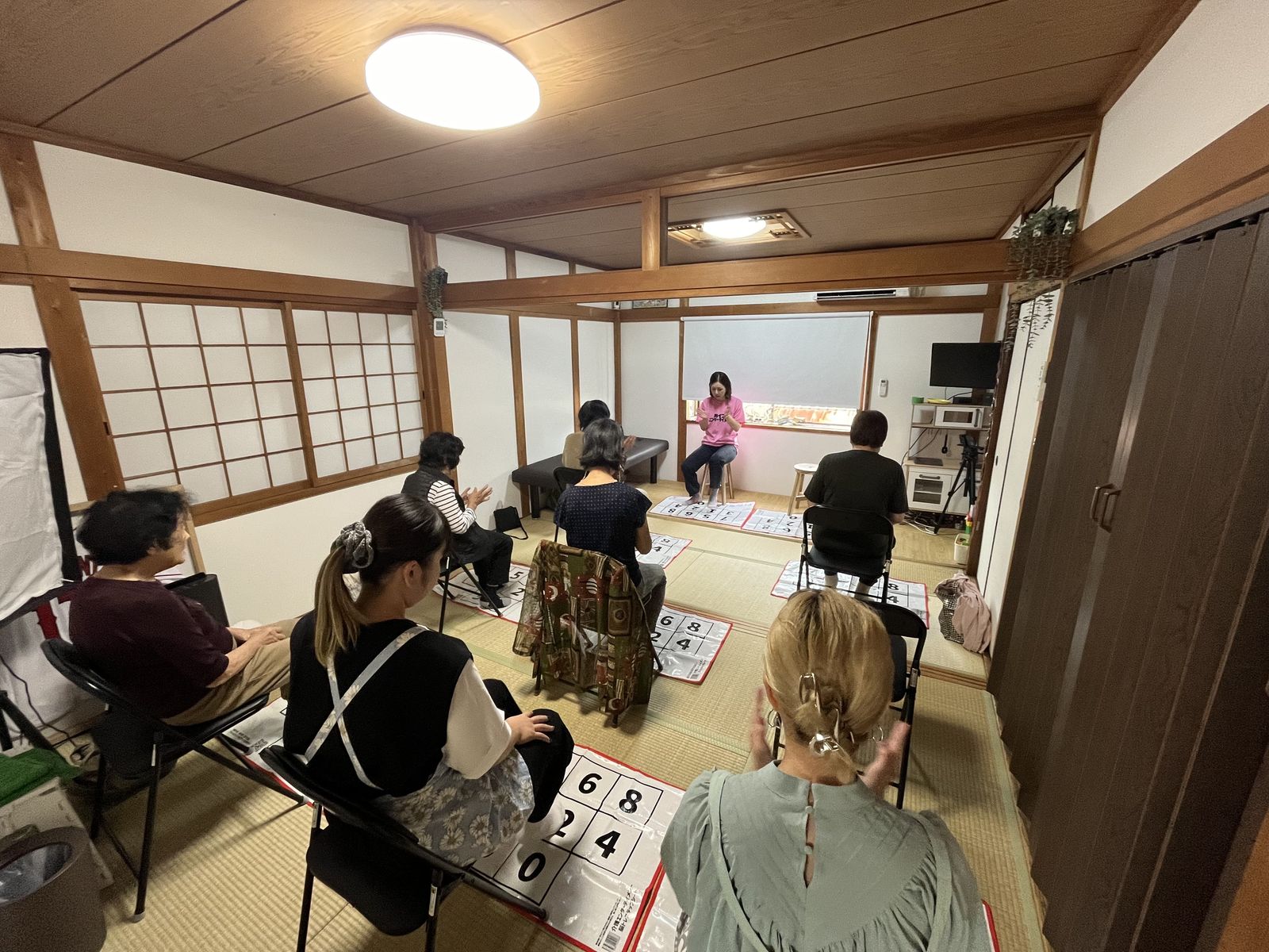和室の公民館で、参加者が脳トレステップシートを使って体操している全景