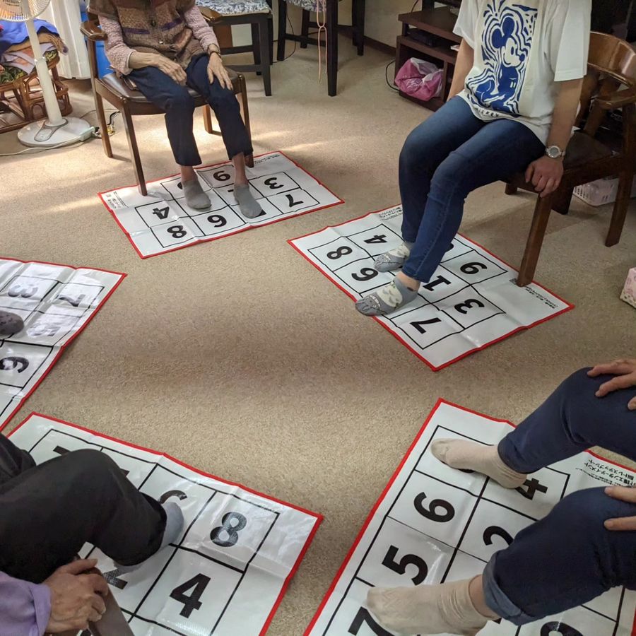 椅子に座った参加者が、足元のシートの数字を足で踏んでいる様子